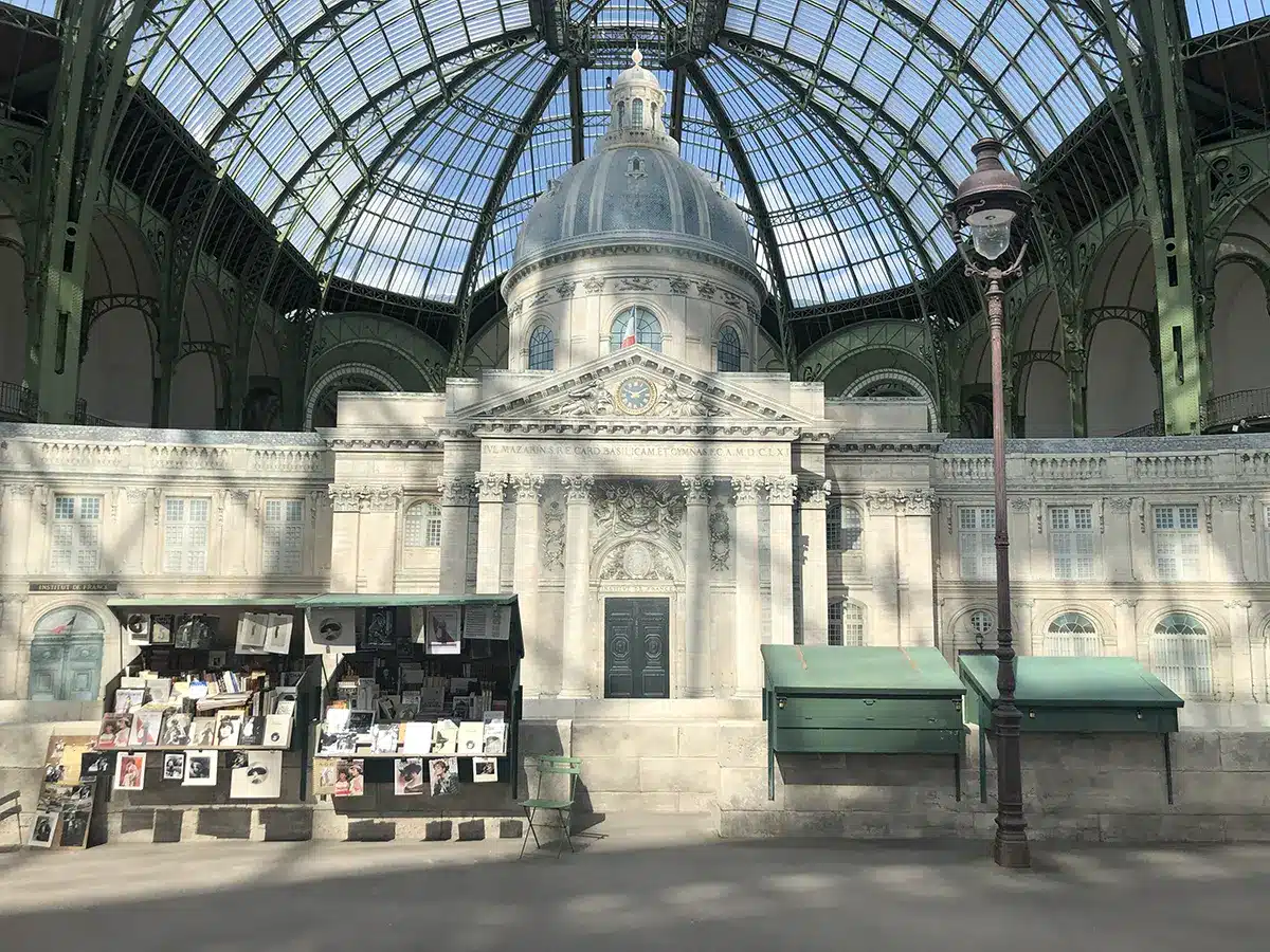 Reconstitution du quai de Seine sous la verrière du Grand Palais, avec la façade de l’Institut de France et ses bouquinistes, créant un décor parisien authentique pour un défilé Chanel.
