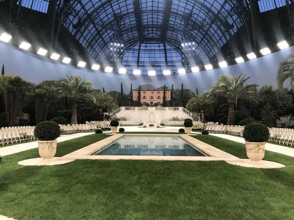 Décor de villa méditerranéenne au Grand Palais, avec piscine centrale, jardins luxuriants, palmiers et ambiance Riviera pour un défilé Chanel.