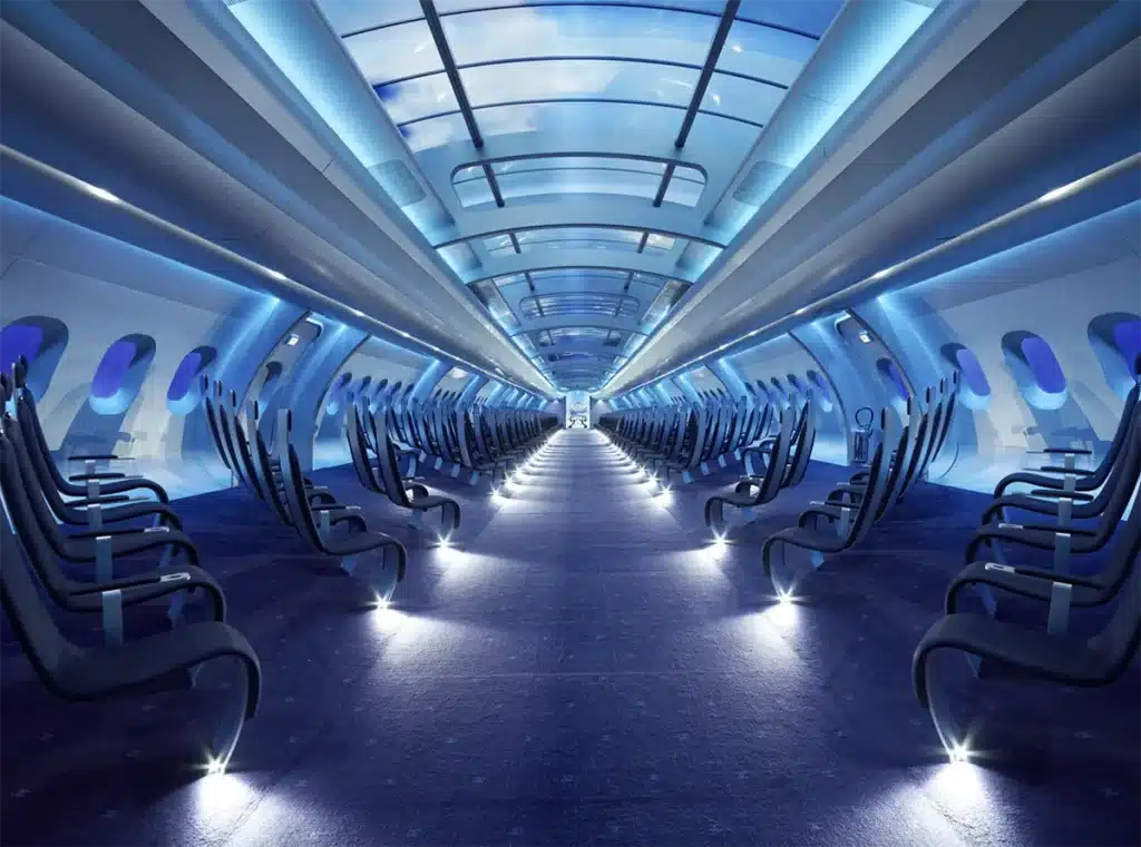 Une cabine futuriste d’avion : rangées de sièges noirs minimalistes, éclairage bleu, et un plafond vitré affichant des images immersives, donnant une ambiance high-tech et irréelle.