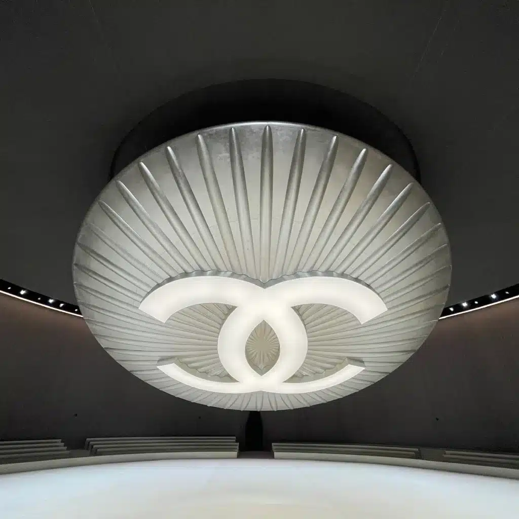 Photo représentant un bouton géant avec le logo Chanel en suspension. Matière argenté et retro éclairé.