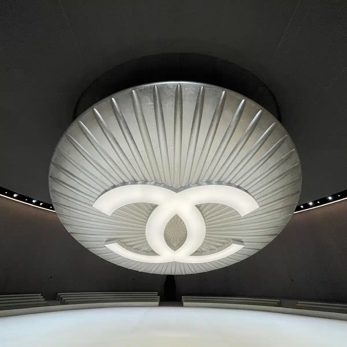 Photo représentant un bouton géant avec le logo Chanel en suspension. Matière argenté et retro éclairé.