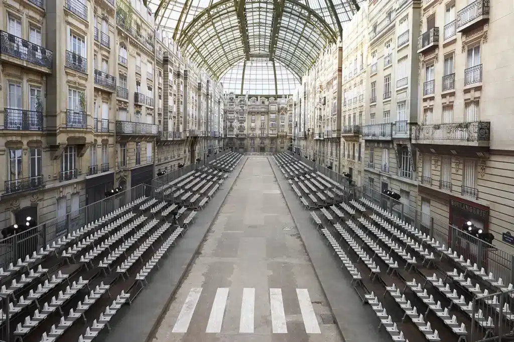 Scénographie du défilé Chanel imaginée sous Karl Lagerfeld, transformant le Grand Palais en rue parisienne grandeur nature. Les façades haussmanniennes, les balcons en trompe-l’œil et la perspective centrale recréent une véritable avenue