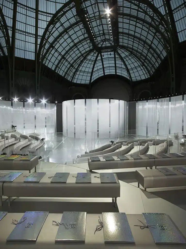 Scénographie futuriste du défilé Haute Couture Chanel 2014 au Grand Palais, imaginée par Karl Lagerfeld : un décor blanc immaculé aux lignes courbes, gradins épurés et ambiance lumineuse cristalline pour une mise en scène élégante et minimaliste.