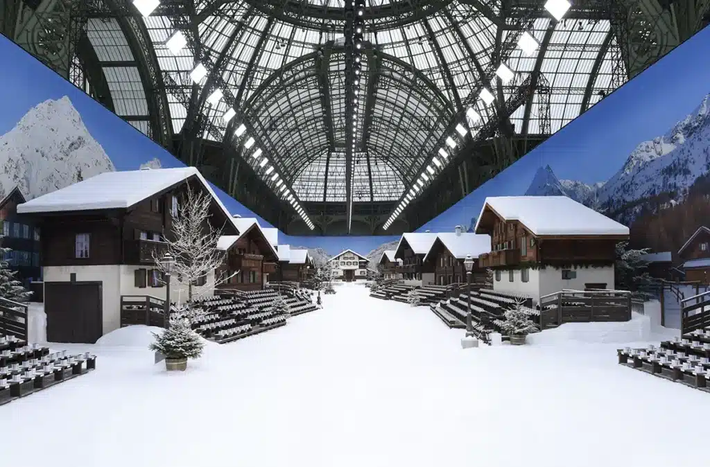 Défilé Chanel au Grand Palais : un décor de village alpin enneigé, avec chalets en bois, allées immaculées et ambiance hivernale recréée sous la majestueuse verrière du Grand Palais.