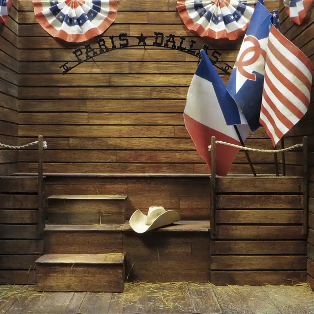 Des petits décors en bois patiné, murs rouges usés, portes battantes de saloon, bottes, chapeaux de cow-boys, drapeaux américains et français, étoiles lumineuses et bottes de foin. L’ensemble évoque l’ambiance Paris–Dallas, mélange de western rétro, de rodeo chic et d’esthétique américaine vintage, avec une touche élégante et théâtrale.