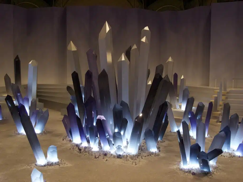 Un paysage spectaculaire de cristaux géants aux teintes violettes, grises et translucides émerge d’un sol scintillant dans une scénographie immersive sous la verrière du Grand Palais, créant une atmosphère futuriste et minérale.