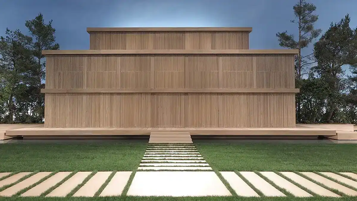 Cette image montre une structure architecturale en bois, épurée et symétrique, évoquant une maison japonaise contemporaine ou un pavillon minimaliste. Le bâtiment, composé de plusieurs niveaux aux lignes rectilignes, repose sur une série de colonnes verticales et d’espaces ouverts qui créent un rythme visuel harmonieux. La façade est entièrement réalisée en bois clair, renforçant l’aspect naturel et zen de l’ensemble. À l’avant, un chemin constitué de larges dalles claires traverse une pelouse parfaitement entretenue pour mener droit à l’entrée centrale. La structure est entourée d’arbres, ce qui ancre le décor dans un environnement paisible et presque méditatif. L’ensemble respire la sobriété, la géométrie et l’équilibre, rappelant certains décors de défilés inspirés par l’architecture traditionnelle asiatique ou par une esthétique de sanctuaire moderne.