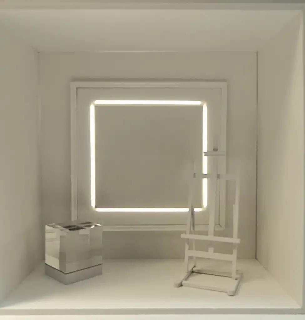 Ces vitrines jouent sur une esthétique minimaliste et lumineuse : un cadre lumineux géométrique structure l’espace, tandis que des volumes transparents ou miroir — cubes, colonnes, socles — mettent en valeur les produits. L’ensemble, très épuré et monochrome, crée une atmosphère contemporaine et presque muséale, où la lumière devient l’élément central de scénographie. Les mannequins, habillés de silhouettes colorées et graphiques, contrastent avec ce décor sobre, renforçant l’effet de mise en scène artistique.