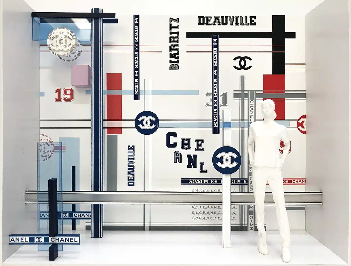 maquettes présentent un univers graphique très structuré, composé de lignes parallèles, bandes colorées et typographies inspirées de plans urbains et de signalétique sportive. Les couleurs principales — rouge, bleu, noir, or et gris — encadrent un mannequin blanc minimaliste placé au centre, mettant en scène l’espace comme une composition graphique en trois dimensions. Les éléments emblématiques de la maison Chanel (logo CC, chiffre 5, numéros 19, 31) surgissent sous forme de blocs en relief. L’ensemble évoque un décor moderne, rythmé et architectural, à la fois ludique et élégant, déployé ensuite en vitrine réelle où les mannequins portent les silhouettes Chanel devant cette cartographie stylisée.