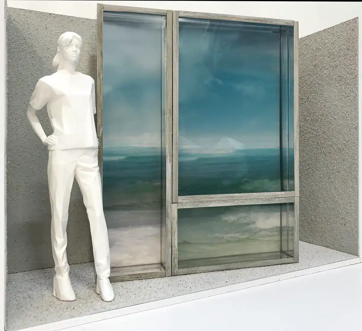 Une mise en scène épurée montrant un mannequin blanc stylisé placé devant un grand panneau évoquant une fenêtre donnant sur la mer. Le décor combine textures minérales gris clair et cadres en bois patiné, créant l’illusion d’un horizon marin calme et lumineux.